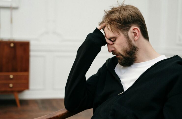 A man sits pensively with his hand on his face, capturing a moment of introspection and stress.