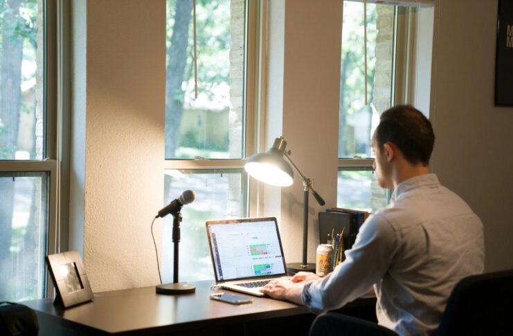 A man working from home, on a laptop and in front of a window.