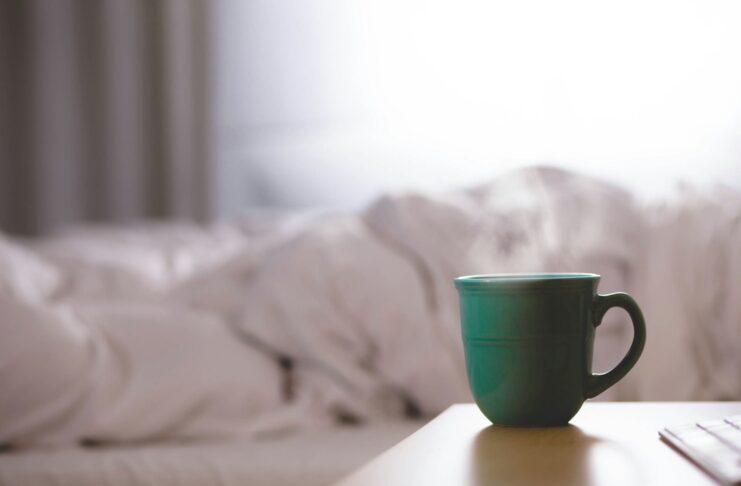 A mug in the foreground and the appearance of a person in bed in the background.