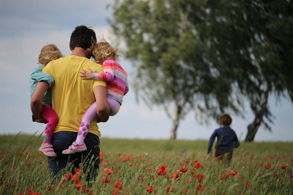 A man carrying small children in a poppy field.