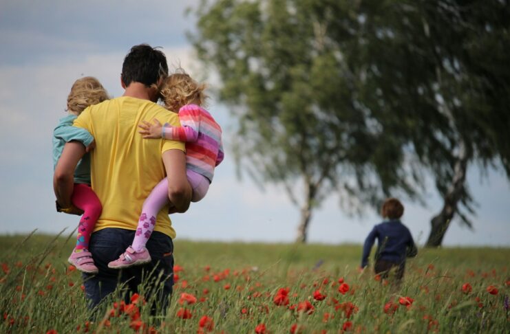 A man carrying small children in a poppy field.