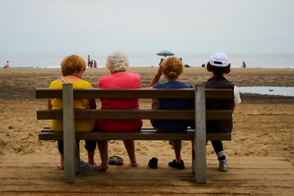 A group of elderly people sitting on a bench at the beach.
