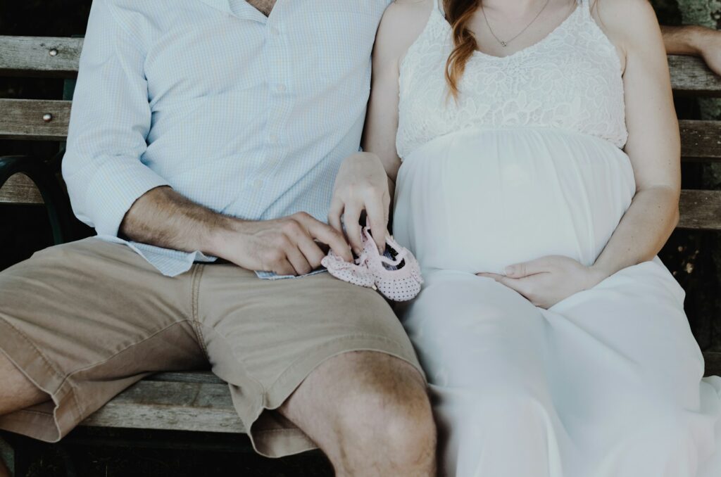 A man and pregnant woman sitting on a bench.