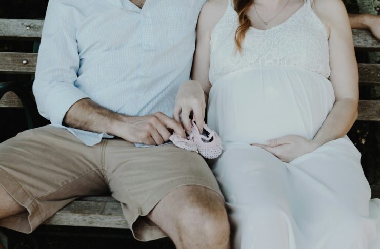 A man and pregnant woman sitting on a bench.