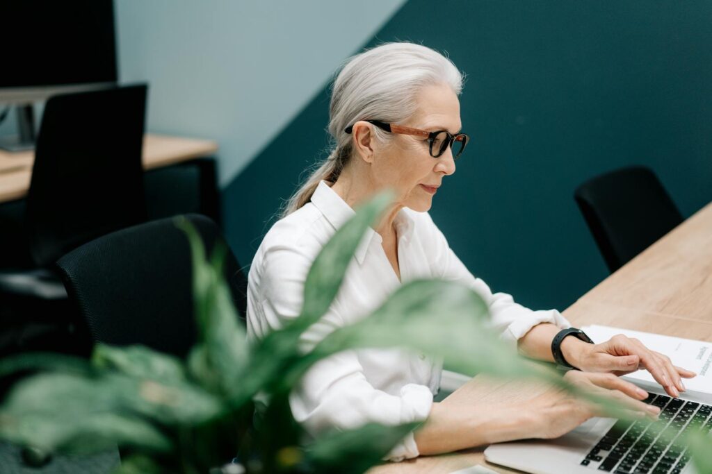 A middle-aged woman with grey hair types on a laptop.