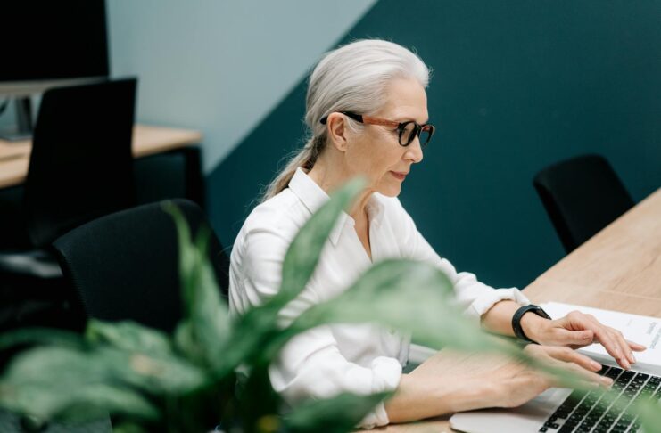A middle-aged woman with grey hair types on a laptop.