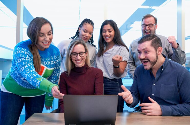 A group of smiling staff gathered around a laptop.