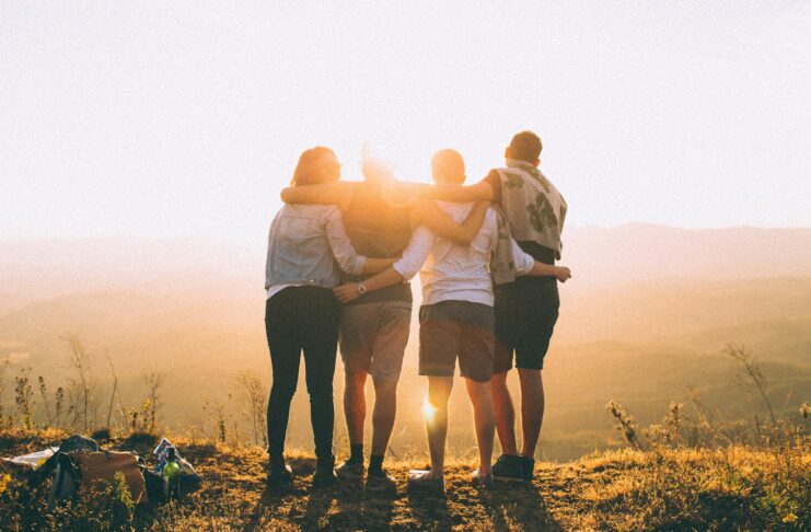 A group of people outside and in front of a sunset.
