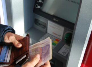 UK Employees ‘Absorb the Hidden Costs of Modern Work’ A person holding brown leather wallet and banknotes at an ATM.