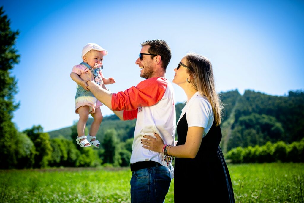 Parents holding a baby aloft in a field.