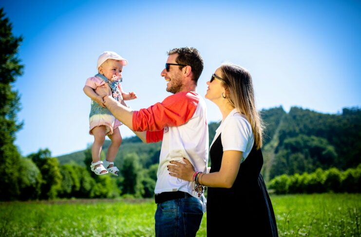 Parents holding a baby aloft in a field.
