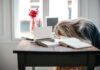 Leaders Recognise Admin Overload But European Employees Are ‘Still Losing Hours Each Week’ Blonde woman slumped over desk with books, showing burnout.