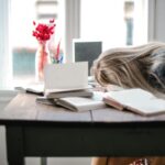 Thriving, Not Surviving: Managing Work-Life Balance Without Burning Out Blonde woman slumped over desk with books, showing burnout.