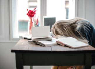 Staff Shortages Continue to Put Pressure on UK Workplaces Blonde woman slumped over desk with books, showing burnout.