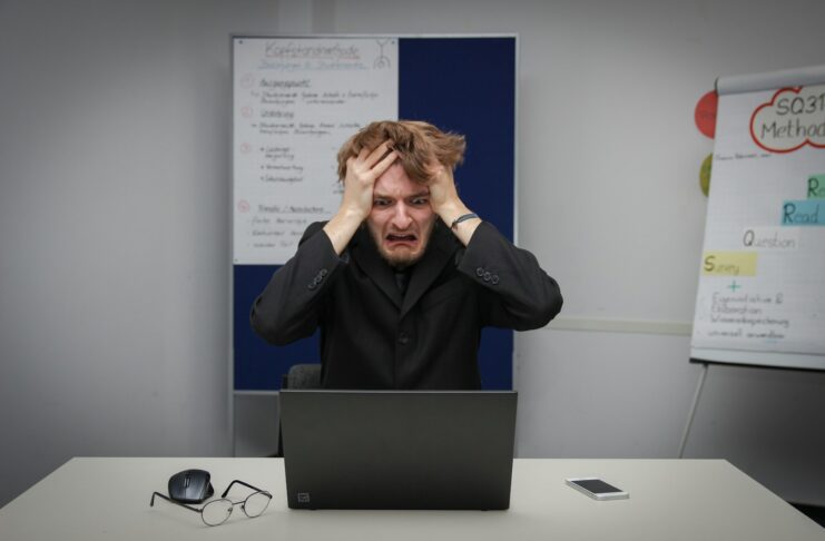 A man sitting in front of a laptop computer and looking stressed.