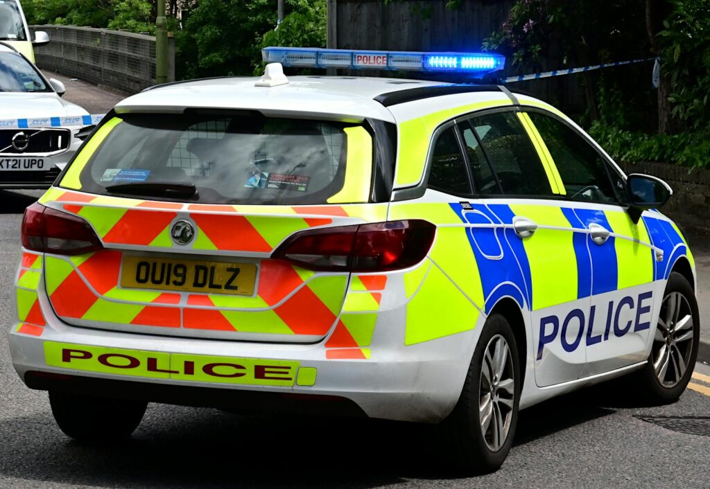 Back view of a British police car with flashing blue lights on a city road, ensuring law enforcement.
