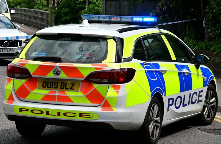 Back view of a British police car with flashing blue lights on a city road, ensuring law enforcement.