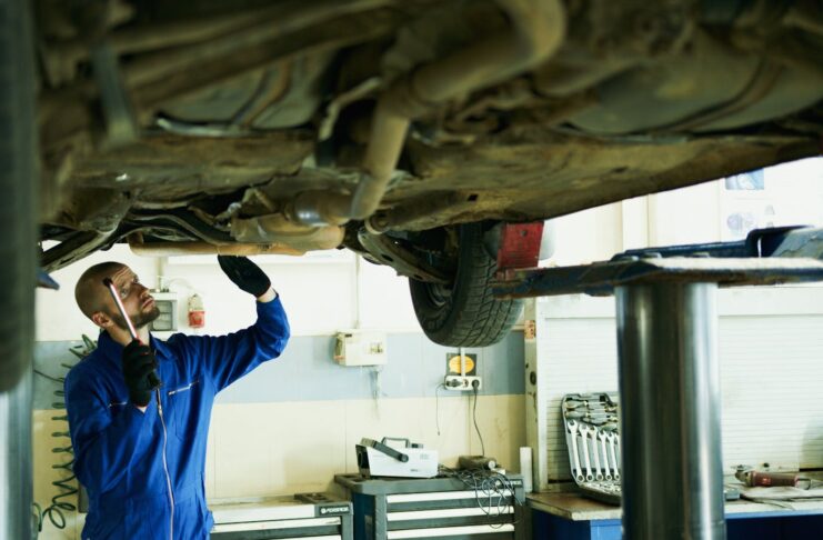 Mechanic inspecting a car's underside in a workshop for repairs.