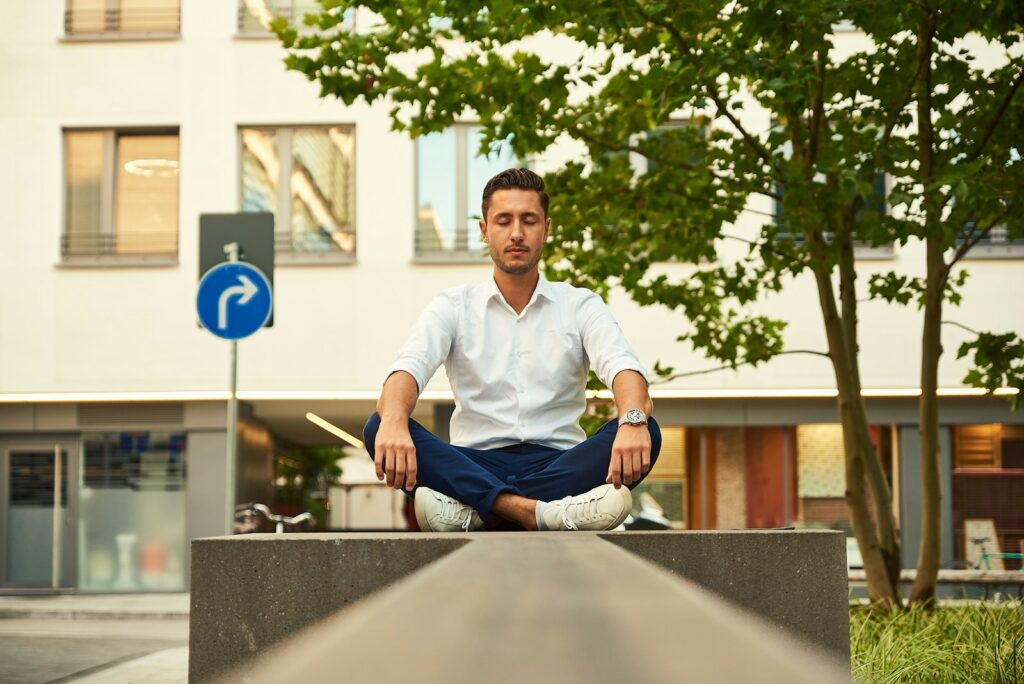 A man sits cross-legged and meditating outside a building.