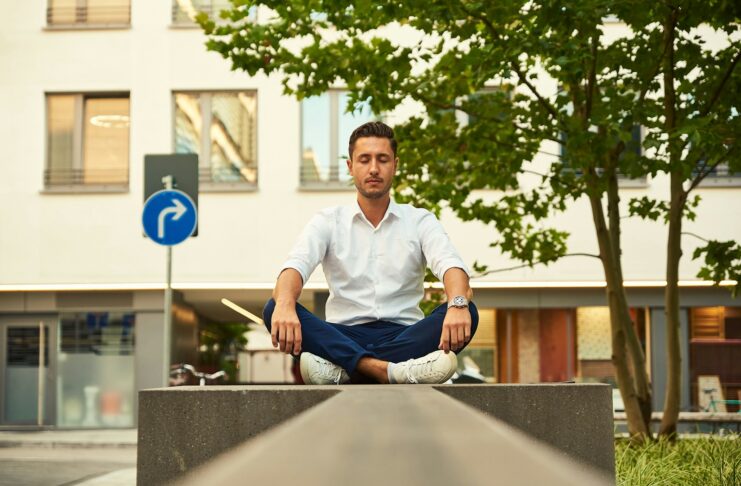 A man sits cross-legged and meditating outside a building.