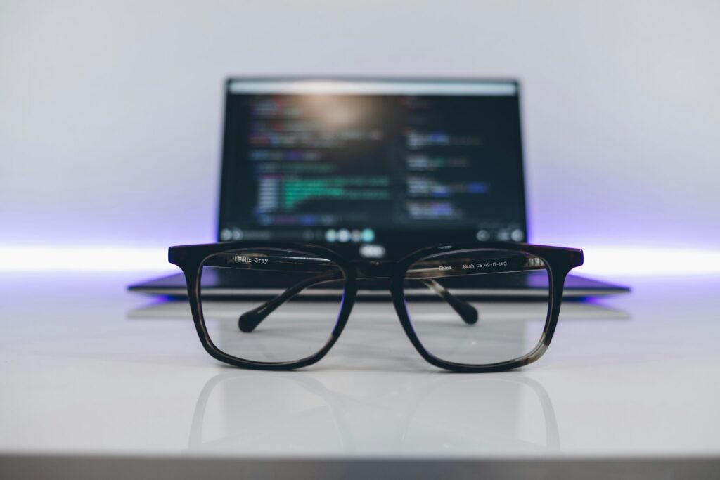 Eyeglasses with black frames on a white desk and in front of a laptop.