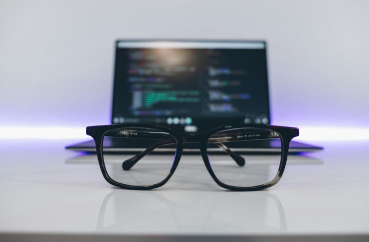 Eyeglasses with black frames on a white desk and in front of a laptop.