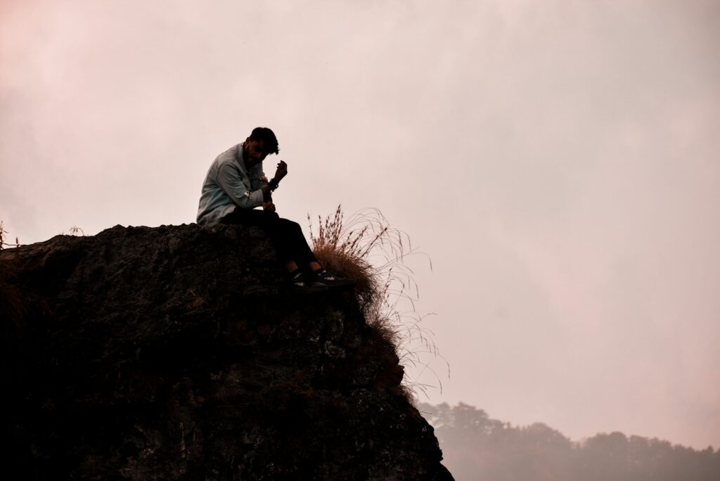 A man sitting on top of a rock next to a grass-covered hillside.