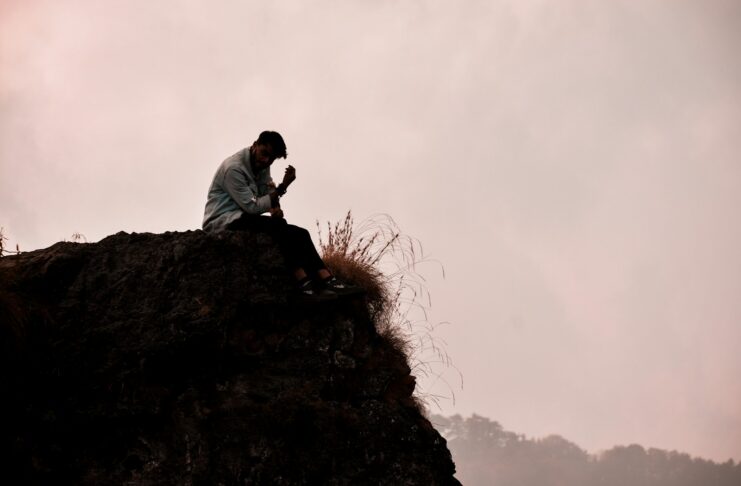 A man sitting on top of a rock next to a grass-covered hillside.