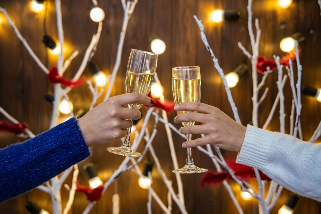Two people toasting with drinks before a Christmas display.