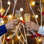 Festive, Not Frazzled: How to Stay Well This Winter Two people toasting with drinks before a Christmas display.