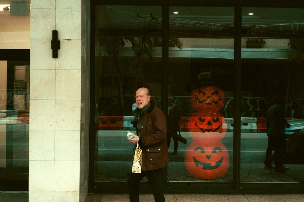 A man walking down a street past a store front with carved Halloween pumpkins in the window.