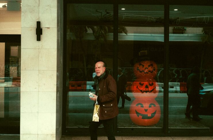 A man walking down a street past a store front with carved Halloween pumpkins in the window.