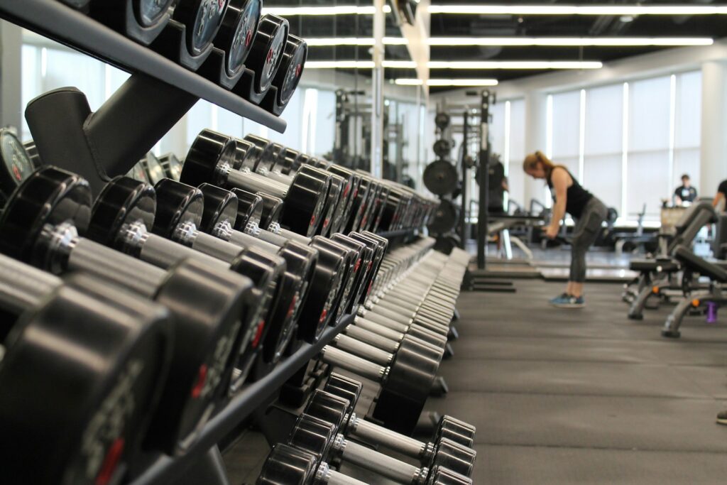 A woman lifts weights at a gym, with a stack of dumbbells at left.