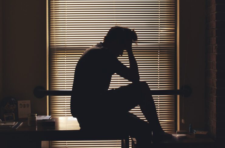 Photo by Adam Custer A man sits on a desk with a hand on his head.