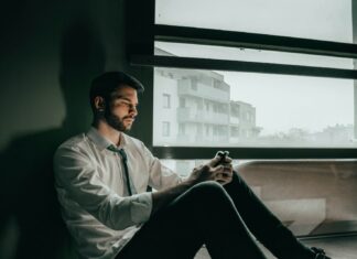 Career Fears Lead Men to Delay Medical Diagnoses A sad man sitting on the floor of an office while looking at his phone.