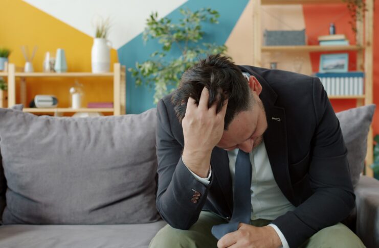 Man in suit sitting on couch with head in hands.