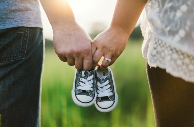 woman and man holding black crib shoes standing near green grass during daytime