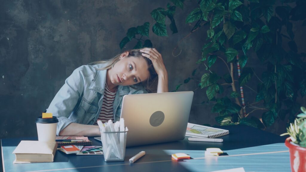 A woman appears stressed while working on a laptop.