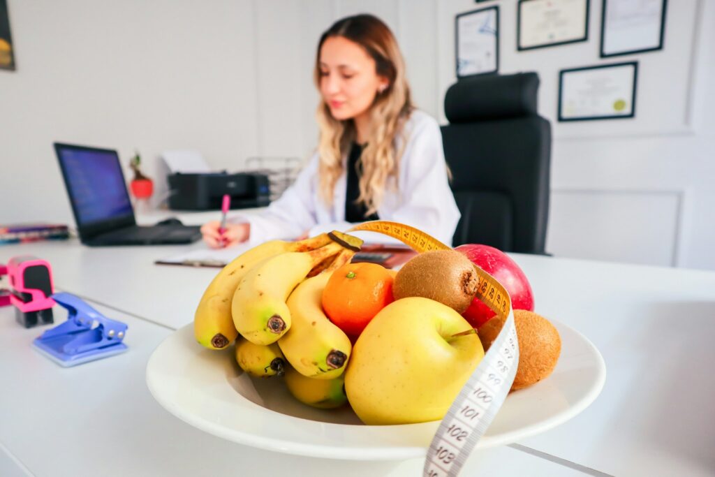 A woman sitting at a desk with a bowl of fruit by her side.
