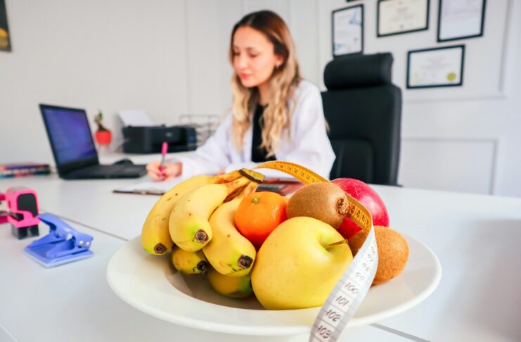 A woman sitting at a desk with a bowl of fruit by her side.