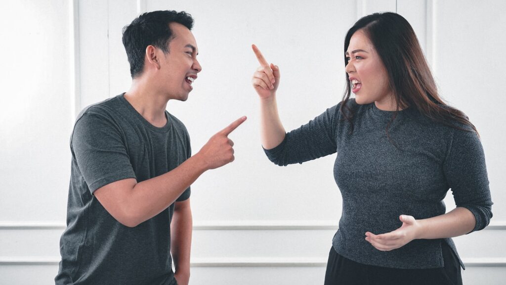 A man and woman pointing at each other and shouting.