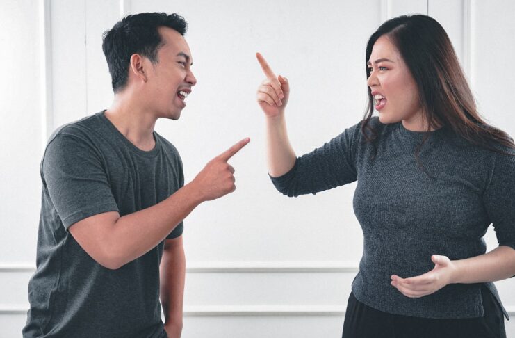 A man and woman pointing at each other and shouting.