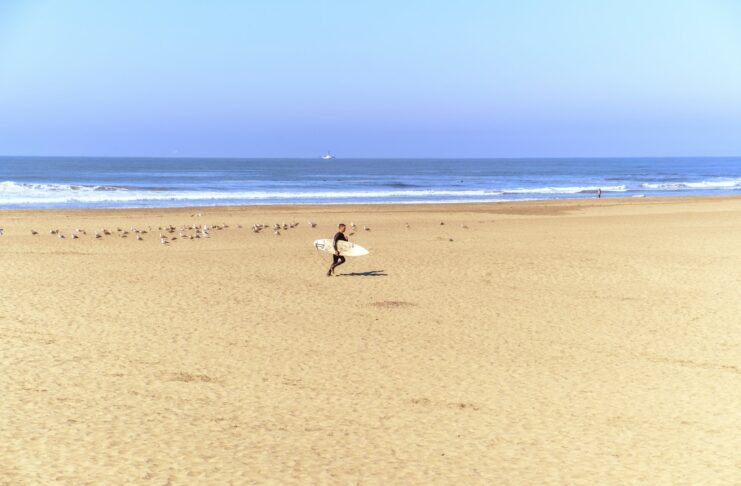 Surfer walks on a beach towards the ocean.