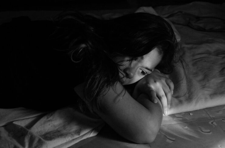 A woman lies on a bed, looking sad.