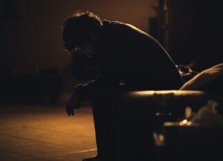 Employers Urged to Lead Recovery as Long-Term Sickness Soars A man sits on a chair, bent over as if ill.