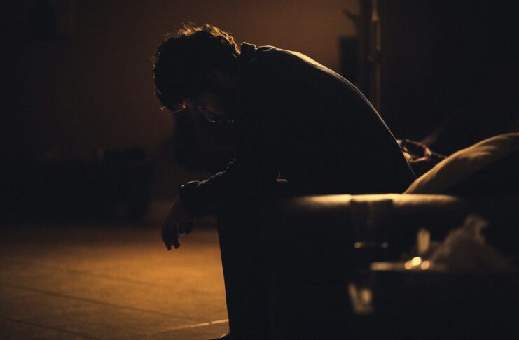 A man sits on a chair, bent over as if ill.
