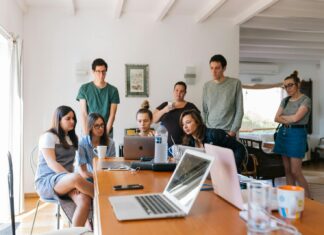 SMEs ‘Consider Pension Provider Switch’ Amid Service Pressure And Wellbeing Concerns Men and women around a long desk in a modern office setting.