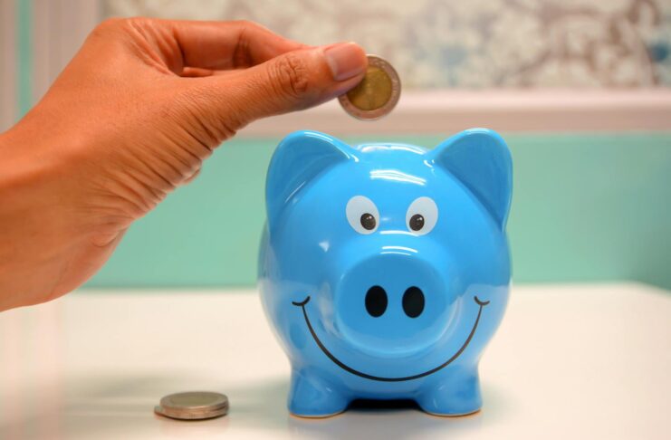 Hand inserting a coin into a blue piggy bank for savings and money management.