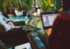 Employers Face Challenge in Meeting Expanding Range of Wellbeing Needs Two individuals working on laptops in a cozy indoor setting surrounded by plants.
