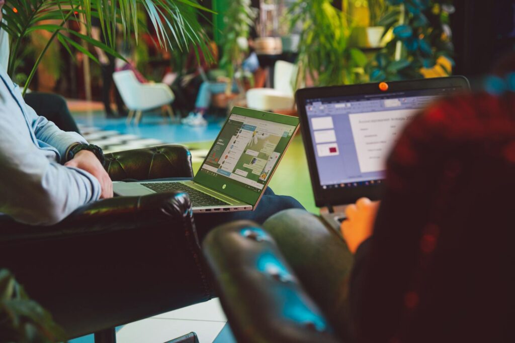 Two individuals working on laptops in a cozy indoor setting surrounded by plants.